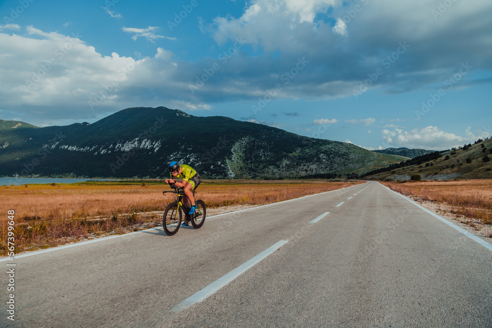Fototapeta premium Full length portrait of an active triathlete in sportswear and with a protective helmet riding a bicycle. Selective focus 