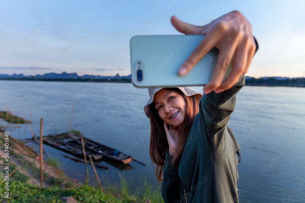 Female tourists smiling and taking selfies with their smartphones against the Mekong River scenery.