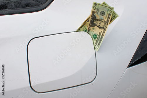 US dollars sitting in a petrol gas tank in the rear of a vehicle. Rise of fuel costs concept shot.