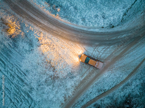 Aerial view of a car driving through a forest at dusk in winter time. Shot taken by a drone. High quality photo