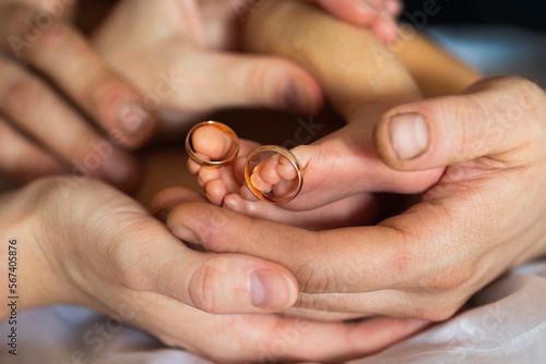 Golden wedding rings on tiny newbornbaby's feet and toes in hands or palms of new parents, mom and dad 
