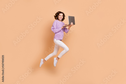 Full length photo of positive pretty lady wear stylish clothes use modern gadget netbook run empty space isolated on beige color background