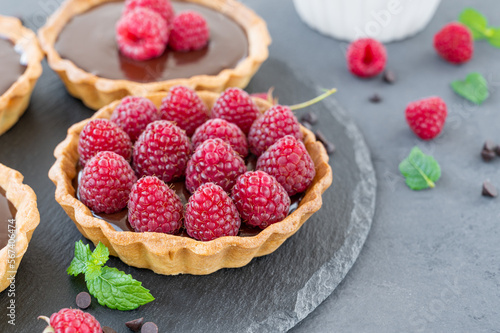 Delicious tart with chocolate cream and fresh raspberry on a gray background. Summer dessert. Copy space.