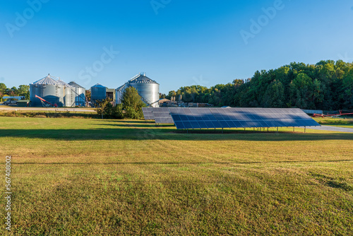 Solar panels on a grain farm with grain bins and a saw mill in the background on a sunny day in Vantown, Tennessee.