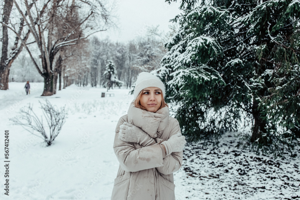 Obraz premium A girl in a beige coat is freezing against the backdrop of a winter forest