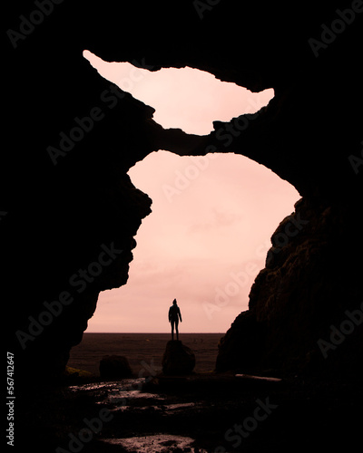 Girl stands on a rock in a famous Yoda cave (Gígjagjá) with beautiful pink sky with clouds. Iceland hidden gems - Hjörleifshöfði mountains