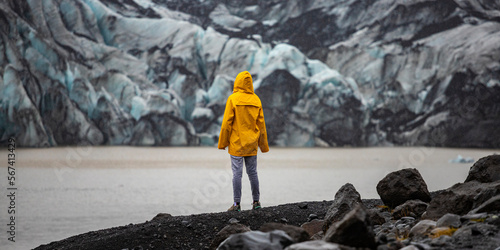 Beautiful girl in a yellow raincoat admires the powerful big Katla glacier during rainy weather in southern Iceland photo