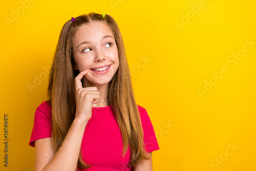 Photo of dreamy schoolgirl with straight hairdo wear pink t-shirt finger near mouth look empty sapce isolated on yellow color background