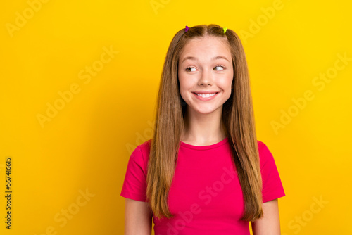 Photo of cute optimistic schoolgirl with straight hairstyle wear pink t-shirt looking empty space isolated on yellow color background