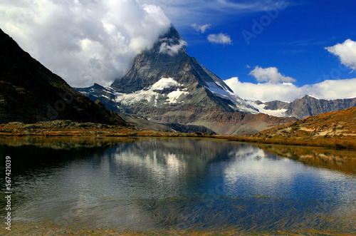 Fototapeta Naklejka Na Ścianę i Meble -  Landscape with a mountain Matterhorn view partially covered by clouds and reflected in the smooth surface of the lake, on a mountain Gornergrat, near Zermatt, in southern Switzerland