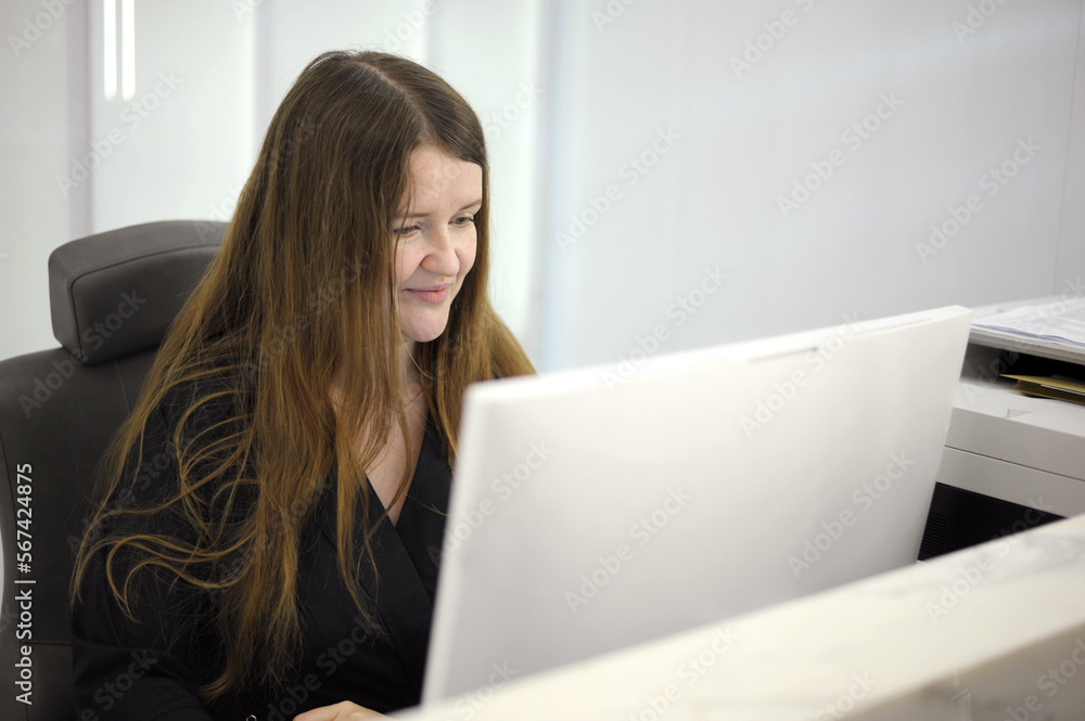 A young woman sits at a computer at the reception of a white light office hospital dentistry any computer programmers long hair black clothes white computer laptop A young woman sits at a computer at the reception of a white light office hospital dentistry any computer programmers long hair black clothes white computer laptop