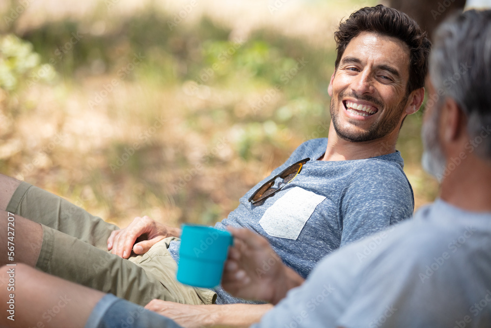 two men who enjoys camping sitting on soft chair two men who enjoys camping sitting on soft chair