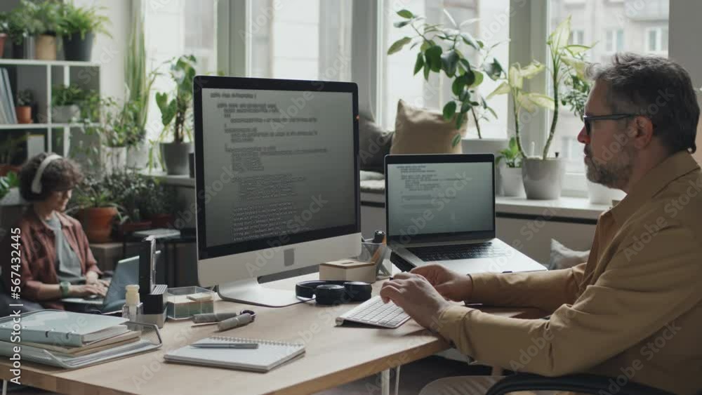 Mature professional programmer working with codes on computer sitting at his workplace in modern office Mature professional programmer working with codes on computer sitting at his workplace in modern office
