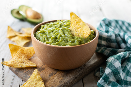 Mexican guacamole with nacho chip in wooden bowl on rustic wooden table. Traditional mexican food.