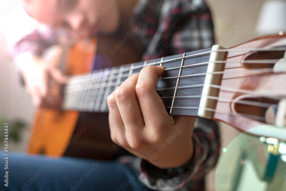 A teenage girl learns to play the guitar. Side view, close-up.