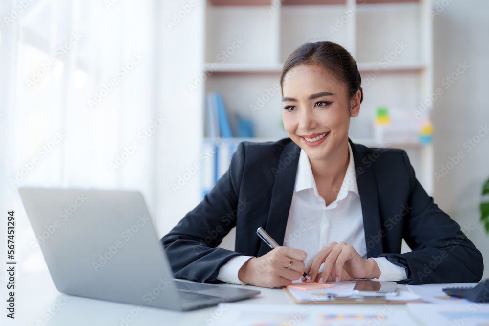 Beautiful Asian businesswoman using her laptop to work and enjoy taking notes on meeting minutes agendas of secretarial work. Beautiful Asian businesswoman using her laptop to work and enjoy taking notes on meeting minutes agendas of secretarial work.