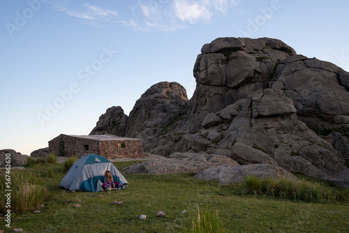 Camping in the top of the rock massif Los Gigantes in Cordoba, Argentina. View of a young woman, tent, Nores refuge and the rocky hills at sunset. 