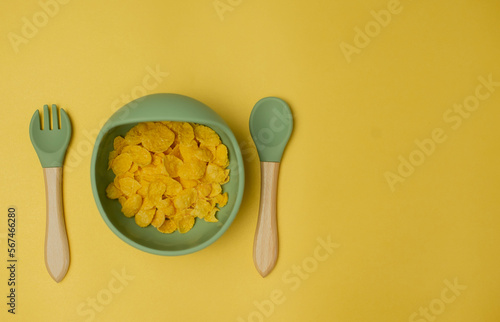 Children's silicone bowl with corn flakes. Baby feeding and nutrition concept. Top view, flat lay.