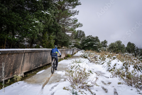 cyclist in the snow next to the water replenishment canal, Gorg Blau reservoir, Escorca, Majorca, Balearic Islands, Spain
