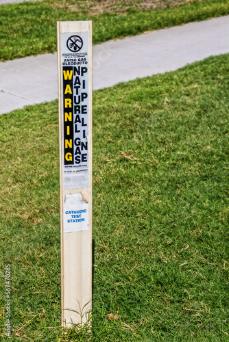 Marker for natural gas pipeline - cathodic test station stuck into green grass by sidewalk - Warning in English and Spanish photo