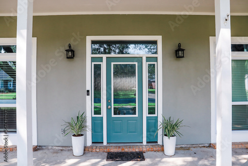A simple walkway to an Acadia style gray house with a turquoise door with transom windows
