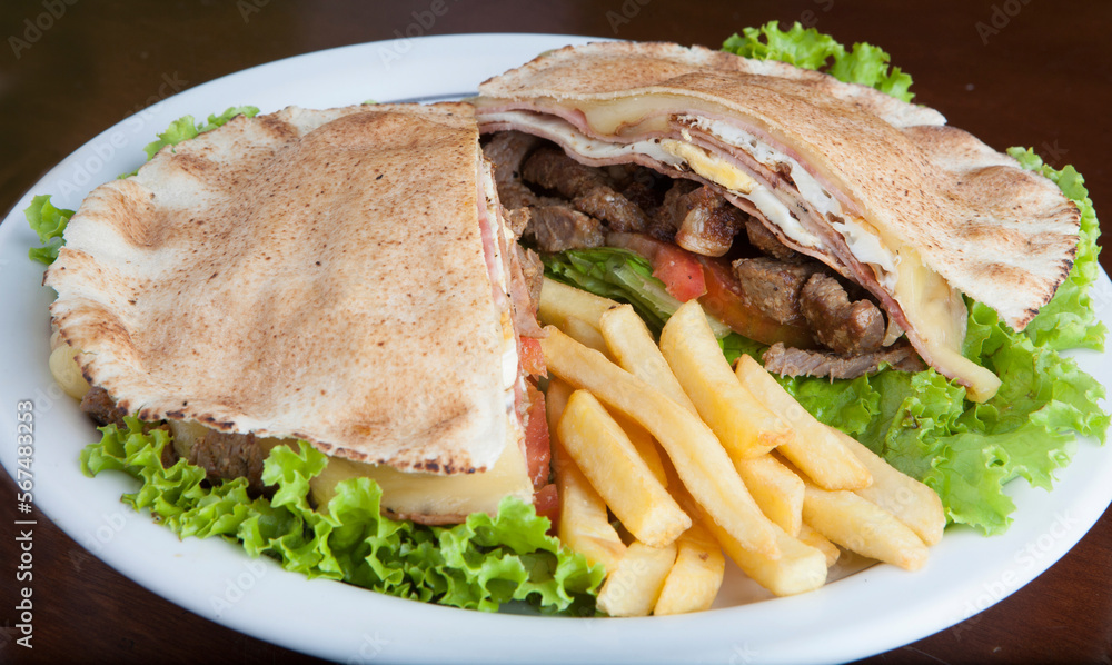 Fototapeta premium Beirut Sandwich Brazilian food recipe libanese flat bread very similar to pita bread, roast beef, slices of muzzarella, slices of tomato curty lettuce leaves, salt, pepper and oregano and french fries