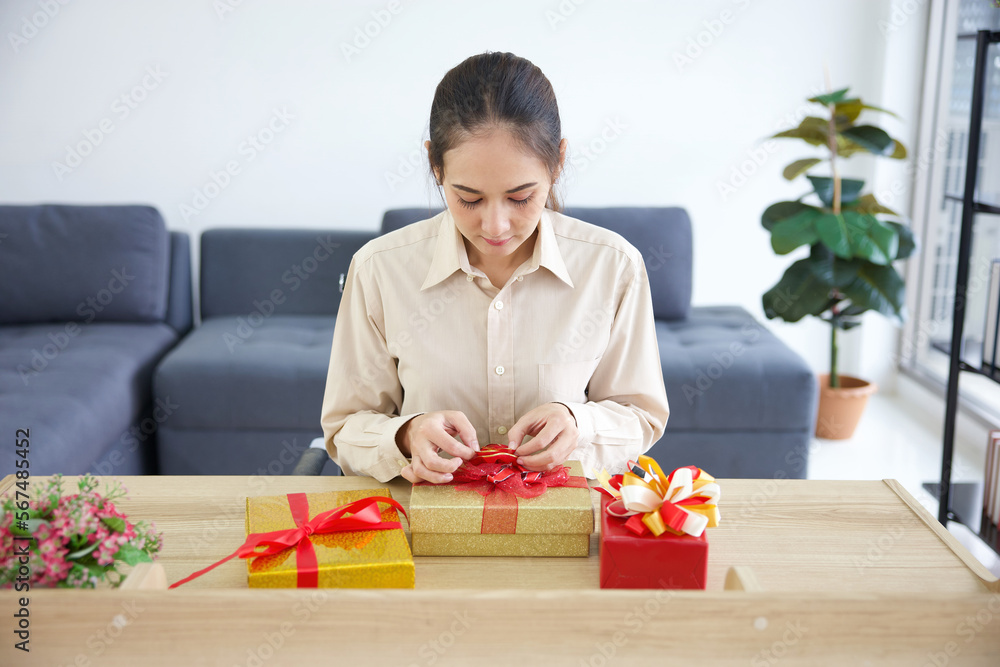 young woman wrapping a gift box on a table in the office young woman wrapping a gift box on a table in the office