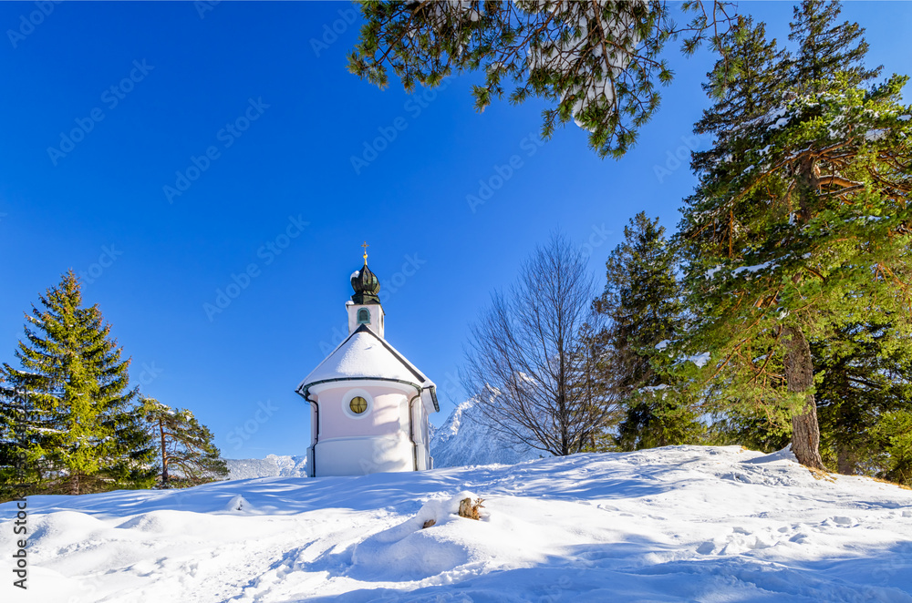 Kleine Kapelle Maria Königin am Lautersee im Schnee mit Kiefern und Tannen vor blauem Himmel