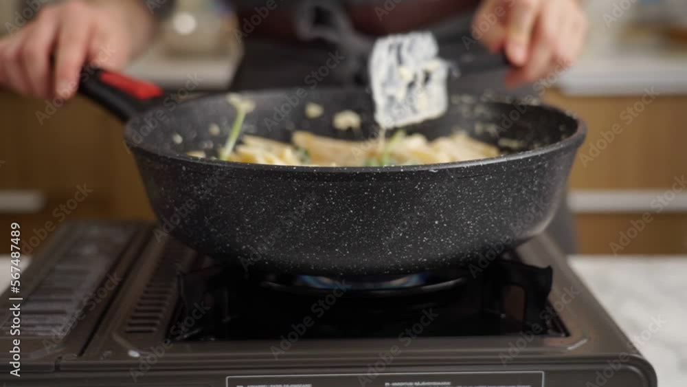 Anonymous cook stirring pasta in frying pan with spatula Anonymous cook stirring pasta in frying pan with spatula