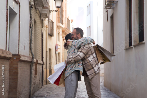 Real marriage of gay couple, hugging on the street, hands full of shopping bags, happy for their gifts. Concept lgtb, lgtbiq+, couples, in love, shopping, sales, hugging. © Manuel