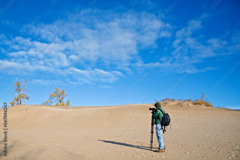 A male photographer taking photos on the sand dune with blue sky and autumn leaf colour A male photographer taking photos on the sand dune with blue sky and autumn leaf colour