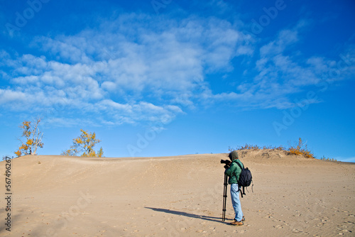 A male photographer taking photos on the sand dune with blue sky and autumn leaf colour