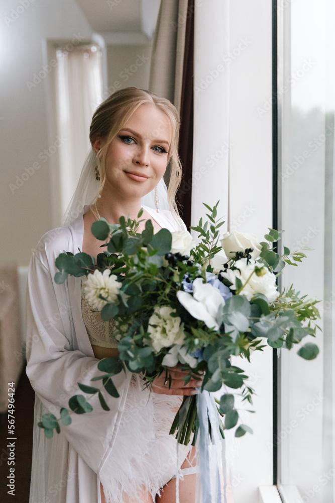 Morning preparations of a beautiful, sexy bride with a wedding bouquet in lingerie, a bathrobe in a hotel, where she puts on shoes in a wedding dress Morning preparations of a beautiful, sexy bride with a wedding bouquet in lingerie, a bathrobe in a hotel, where she puts on shoes in a wedding dress