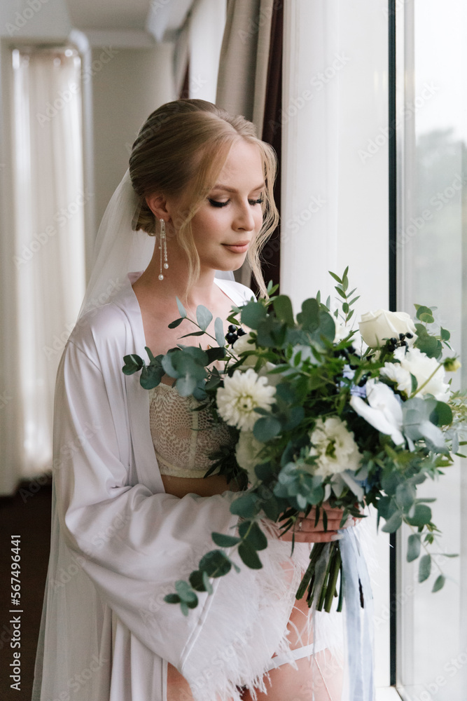 Morning preparations of a beautiful, sexy bride with a wedding bouquet in lingerie, a bathrobe in a hotel, where she puts on shoes in a wedding dress Morning preparations of a beautiful, sexy bride with a wedding bouquet in lingerie, a bathrobe in a hotel, where she puts on shoes in a wedding dress