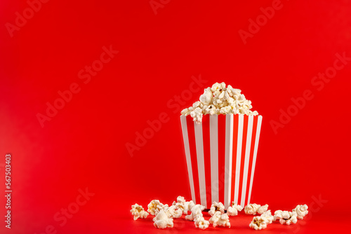 Popcorn in a red and white striped bag on a red background. Front view, copy space.