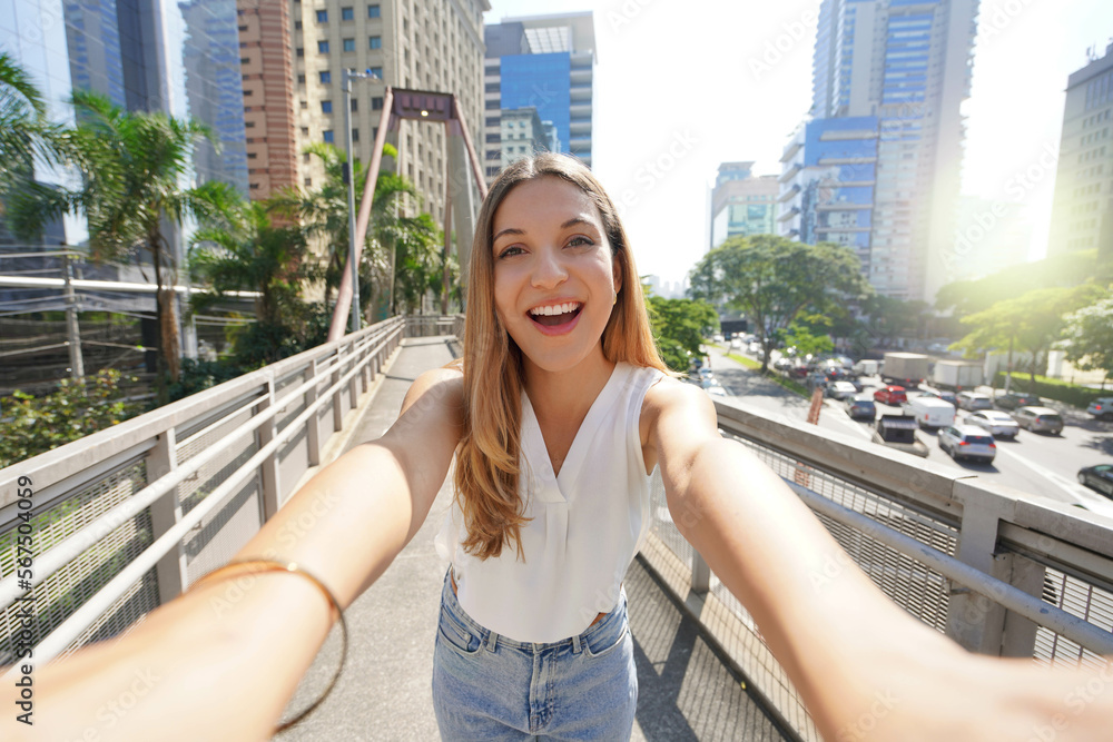 Fototapeta premium Tourism in Sao Paulo. Beautiful smiling girl takes self portrait in Moema financial district of Sao Paulo, Brazil.