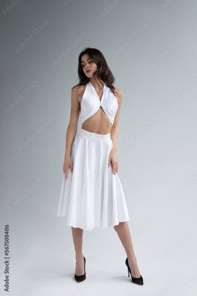 Full length view of young woman with hairstyle in white long dress posing sensual in studio, grey background. Full length view of young woman with hairstyle in white long dress posing sensual in studio, grey background.
