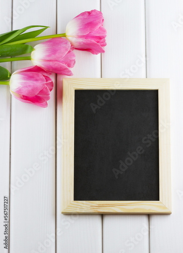 Top view of pink tulips with empty blackboard on white wooden background