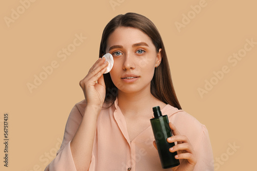 Beautiful woman takes off her make up while holding cotton disk and cleanser. photo