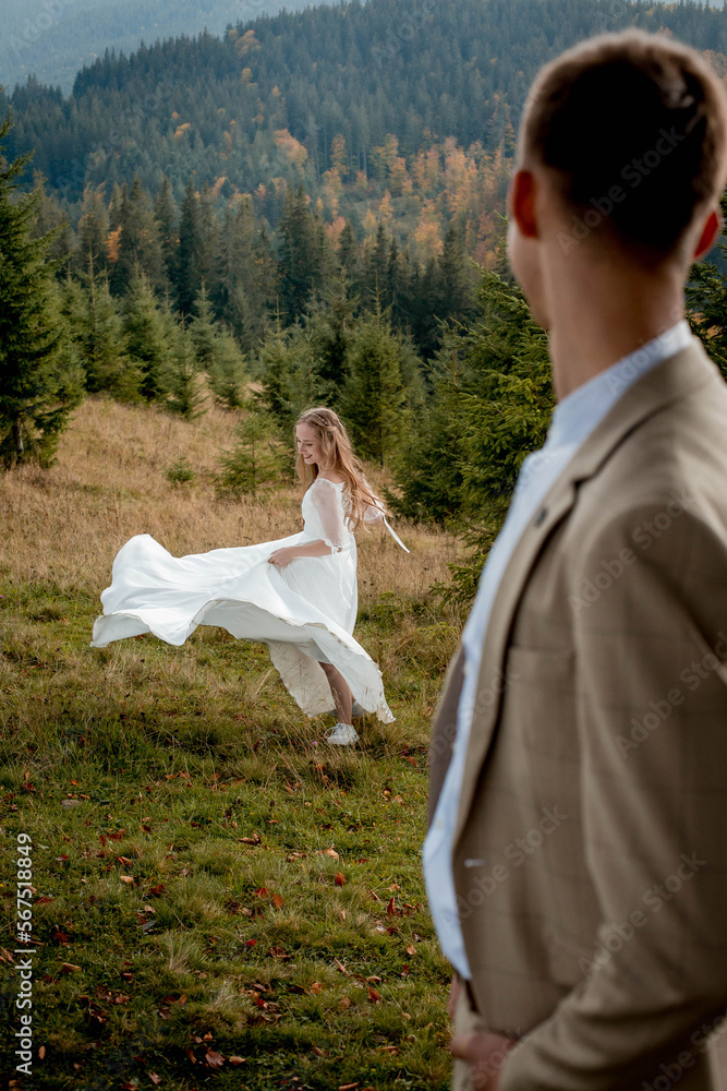 The bride is circling in her wedding dress, and the groom is looking at her. Wedding photo session in the mountain