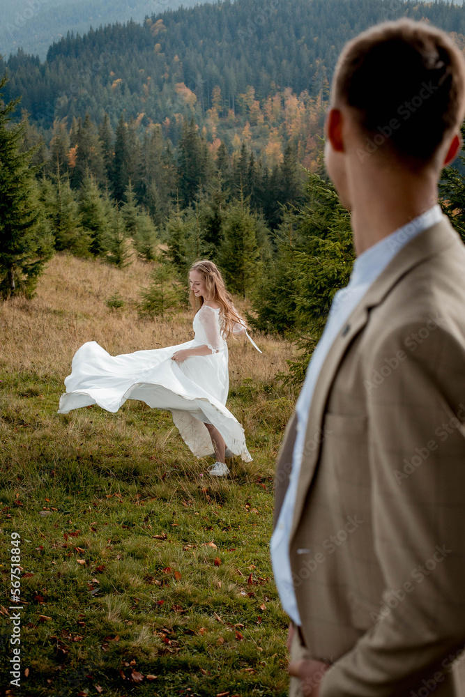 The bride is circling in her wedding dress, and the groom is looking at her. Wedding photo session in the mountain The bride is circling in her wedding dress, and the groom is looking at her. Wedding photo session in the mountain