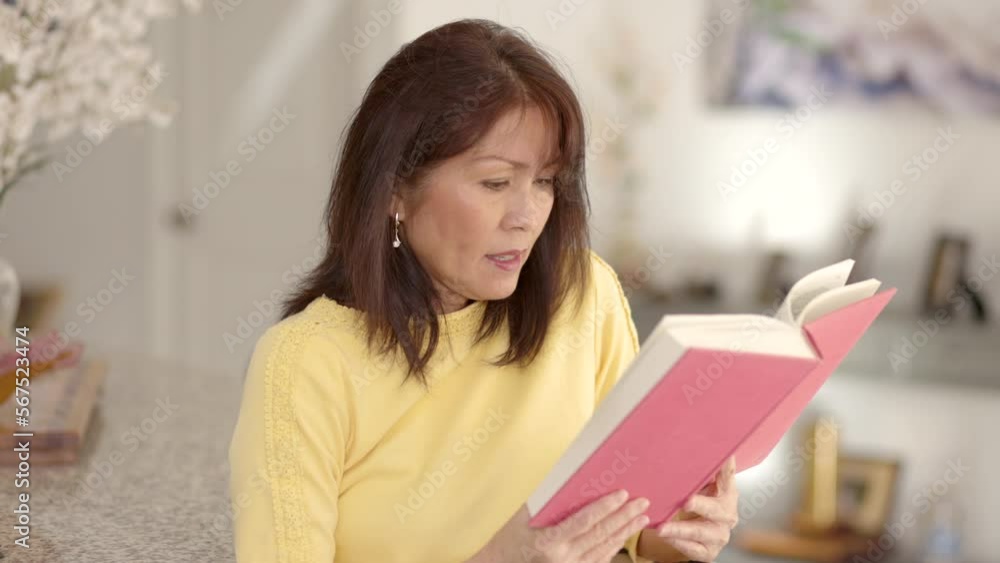 Attractive mature asian woman relaxing reading book sitting in casual leisure home living room chair Attractive mature asian woman relaxing reading book sitting in casual leisure home living room chair