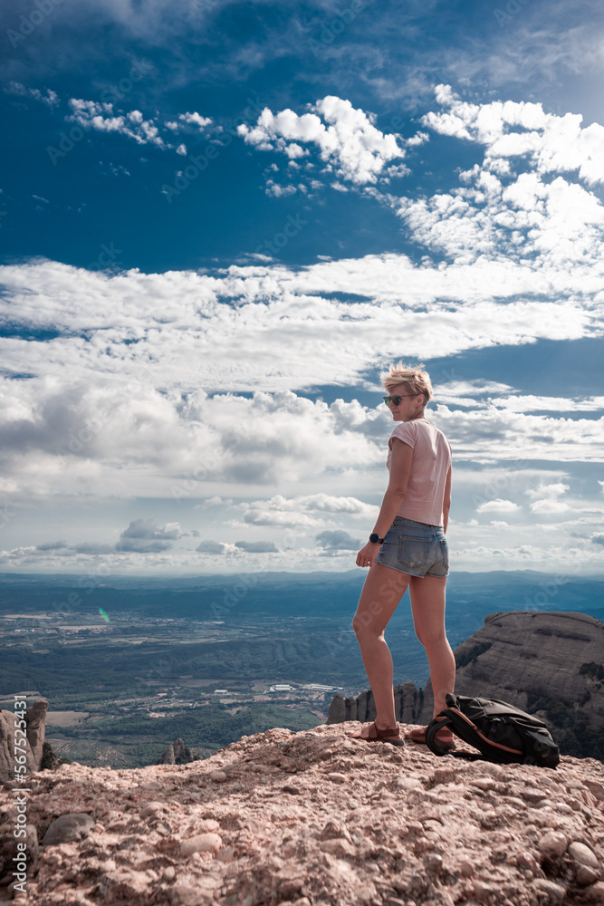 Shot of female hiker on top of Montserrat mountain in Spain. Traveler woman standing on a stone looking at the view.