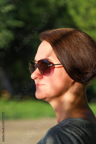 Woman with short hair and in sunglasses in a park on a sunny day. Summer outdoor leisure