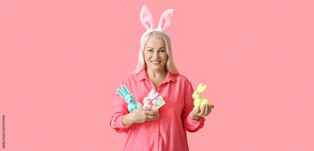 Mature woman with bunny ears and toy rabbits on pink background. Easter celebration Mature woman with bunny ears and toy rabbits on pink background. Easter celebration