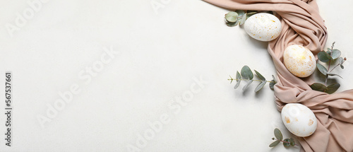 Beautiful Easter eggs, eucalyptus branches and cloth on light background with space for text