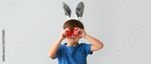 Cute little boy with bunny ears and Easter eggs on grey background