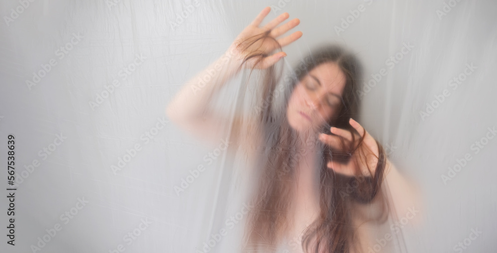 Fototapeta premium banner blurred, fuzzy image of sensual romantic young naked woman portrait behind plastic film, looking down, playing shy with her hair, moves in ecstasy