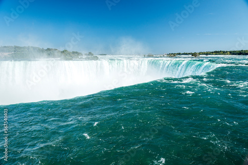 The greenish blue water at the brink of the Horseshoe Falls in Niagara Falls Ontario Canada. Mist from the falls rises in the distance.