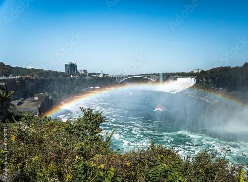 A boat passes through the mist from the Falls under a rainbow in Niagara Falls Canada. The Rainbow Bridge  an international border crossing  joins Canada and the United States is in the distance.